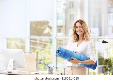 Young beautiful businesswoman holding yoga mat in office. Gym after work - Powered by Shutterstock