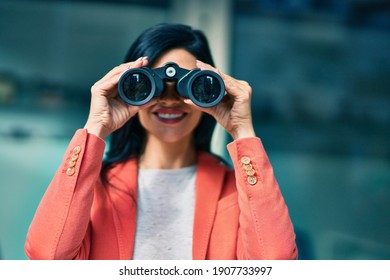 Young beautiful businesswoman smiling happy looking for new opportunities using binoculars at the city. - Powered by Shutterstock