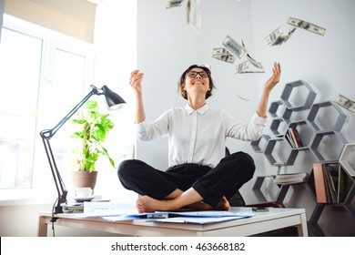 Young beautiful businesswoman throwing up money, sitting on table.