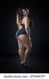 Young beautiful busty curvy caucasian plus size model in swimsuit, xxl woman on black background, full length portrait