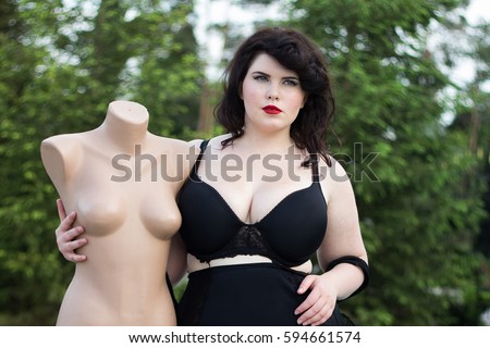 Young beautiful busty curvy  plus size model with big breast in black bra holding mannequin, xxl woman, professional makeup and hairstyle