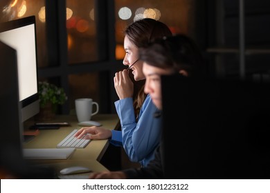 Young And Beautiful Call Center Officers Team Work Overtime With Happy At 24/7 Hour At Night With Bokeh Of Light In Background. Concept For Customer Service Late Working For Support As Back Office.