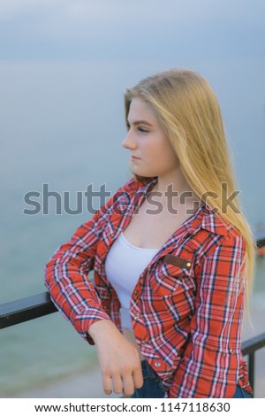 young beautiful calm girl are looking at the sea horizon, young blond woman stands with her back, teen girl hipster in red shirt.