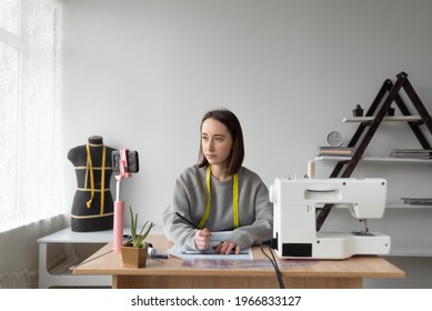 Young Beautiful Caucasian Girl Seamstress Conducts Training For Designers. Sits By The Table. Online Lesson, Distance Education. Copy Space.