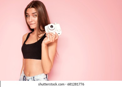 Young beautiful caucasian girl taking photos, posing on pink background.