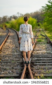 Young And Beautiful Caucasian Girl Walking On A Railway That Splits In Two Directions, Concept About Choosing A Direction In Life, Weighing The Decision To Follow A Certain Path To The Future.