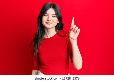 Young beautiful caucasian girl wearing casual red shirt smiling with an idea or question pointing finger up with happy face, number one 