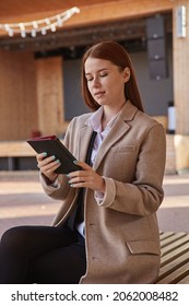 Young Beautiful Caucasian Woman In Beige Stylish Coat Using Tablet Outdoors On Sunny Day, Reading Ebook. Attractive Female Street Portrait At Fall Or Spring. Autumn Lifestyle, Modern Technology