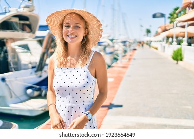 Young beautiful caucasian woman with blond hair smiling happy outdoors on a summer day walking by the nautical port