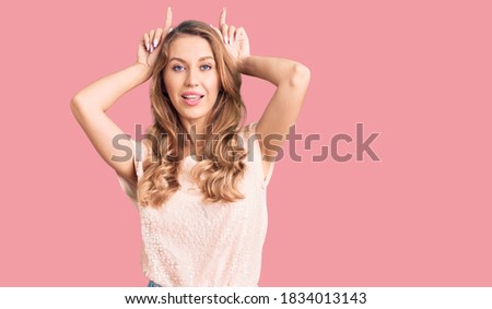 Young beautiful caucasian woman with blond hair wearing casual clothes doing funny gesture with finger over head as bull horns 