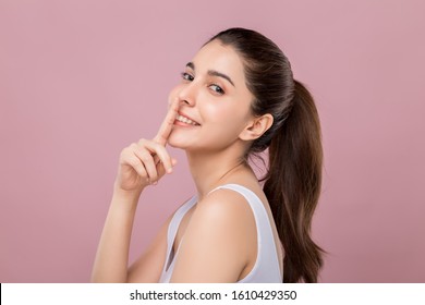 Joven y hermosa mujer caucásica con cara sonriente tocando su nariz, concepto de trabajo de cirugía nasal, aislada en un fondo rosado.