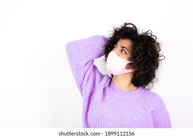 Young Beautiful Caucasian Woman Wearing Pink Medical Mask Standing Against White Wall, Confuse And Wonder About Question. Uncertain With Doubt, Thinking With Hand On Head. Pensive Concept.