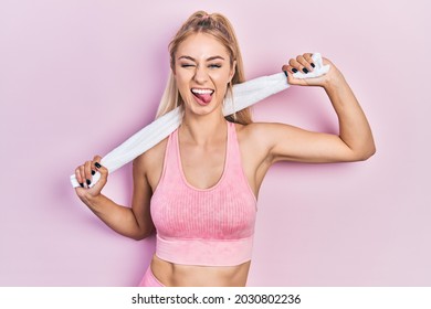 Young beautiful caucasian woman wearing sportswear and towel sticking tongue out happy with funny expression. 