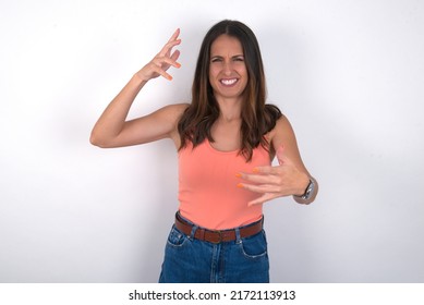 young beautiful caucasian woman wearing orange top over white background Shouting frustrated with rage, hands trying to strangle, yelling mad.