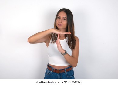 young beautiful caucasian woman wearing white top over white background feels tired and bored, making a timeout gesture, needs to stop because of work stress, time concept.