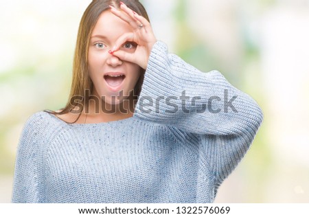 Young beautiful caucasian woman wearing winter sweater over isolated background doing ok gesture shocked with surprised face, eye looking through fingers. Unbelieving expression.