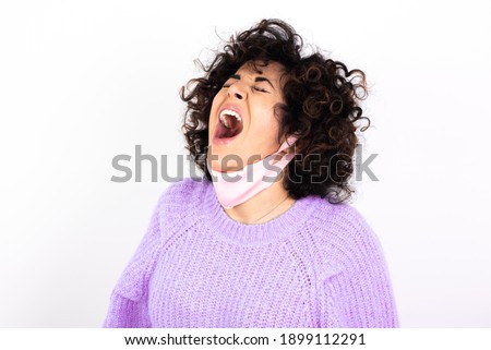 young beautiful caucasian woman wearing pink medical mask standing against white wall, angry and mad screaming frustrated and furious, shouting with anger. Rage and aggressive concept.