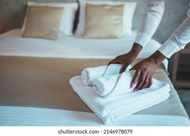 Young beautiful chambermaid in uniform holding stack of clean folded towels while going to put them on changed bed in hotel room.  Photos in the interior. - Shutterstock ID 2146978079
