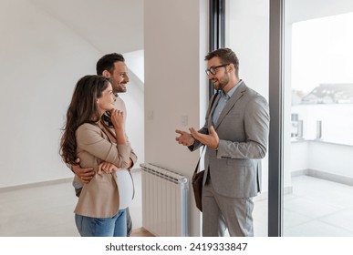 A young, beautiful, cheerful couple expecting a baby, talking with a real-estate agent visiting apartment for sale or for rent. Future parents buying an apartment. Real estate concept. A new beginning - Powered by Shutterstock