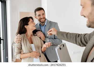 A young, beautiful, and cheerful couple,  a man and his pregnant wife, talking with a real-estate agent visiting apartment for sale or for rent. Future parents buying an apartment. Real estate concept - Powered by Shutterstock