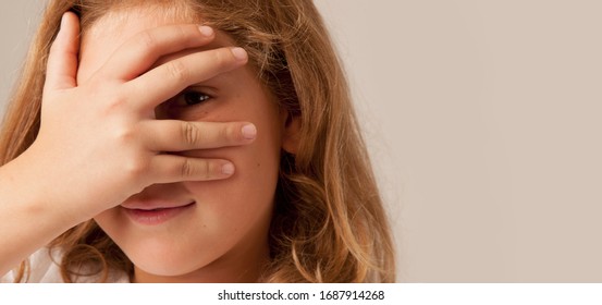 Young beautiful child girl peeking behind her hand and finger as a symbol of trickery and deceit.