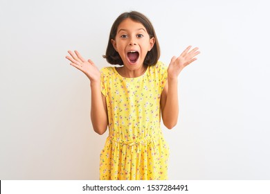 Young Beautiful Child Girl Wearing Yellow Floral Dress Standing Over Isolated White Background Celebrating Crazy And Amazed For Success With Arms Raised And Open Eyes Screaming Excited. Winner Concept