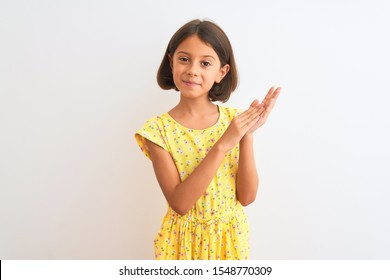 Young Beautiful Child Girl Wearing Yellow Floral Dress Standing Over Isolated White Background Clapping And Applauding Happy And Joyful, Smiling Proud Hands Together