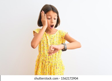 Young Beautiful Child Girl Wearing Yellow Floral Dress Standing Over Isolated White Background Looking At The Watch Time Worried, Afraid Of Getting Late