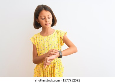 Young Beautiful Child Girl Wearing Yellow Floral Dress Standing Over Isolated White Background Checking The Time On Wrist Watch, Relaxed And Confident