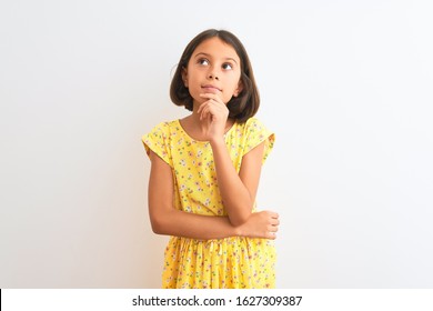 Young Beautiful Child Girl Wearing Yellow Floral Dress Standing Over Isolated White Background With Hand On Chin Thinking About Question, Pensive Expression. Smiling With Thoughtful Face. Doubt