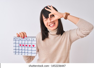 Young Beautiful Chinese Woman Holding Menstruation Calendar Over Isolated White Background With Happy Face Smiling Doing Ok Sign With Hand On Eye Looking Through Fingers