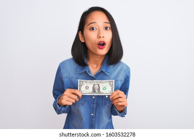 Young Beautiful Chinese Woman Holding One Dollar Standing Over Isolated White Background Scared In Shock With A Surprise Face, Afraid And Excited With Fear Expression