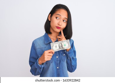 Young Beautiful Chinese Woman Holding One Dollar Standing Over Isolated White Background Serious Face Thinking About Question, Very Confused Idea