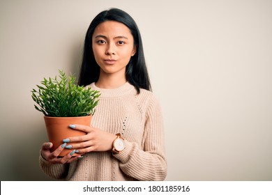 Young Beautiful Chinese Woman Holding Plant Pot Standing Over Isolated White Background With A Confident Expression On Smart Face Thinking Serious