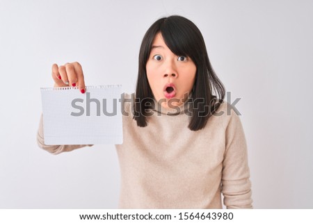 Young beautiful chinese woman holding notebook over isolated white background scared in shock with a surprise face, afraid and excited with fear expression