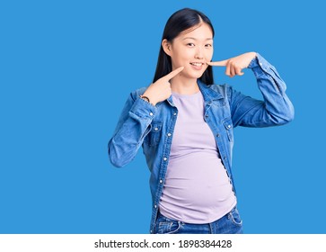 Young Beautiful Chinese Woman Pregnant Expecting Baby Smiling Cheerful Showing And Pointing With Fingers Teeth And Mouth. Dental Health Concept. 