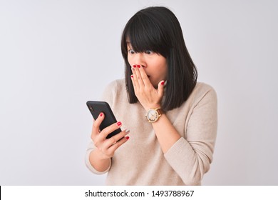 Young beautiful Chinese woman using smartphone standing over isolated white background cover mouth with hand shocked with shame for mistake, expression of fear, scared in silence, secret concept