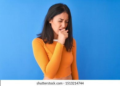 Young Beautiful Chinese Woman Wearing Orange T-shirt Standing Over Isolated Blue Background Feeling Unwell And Coughing As Symptom For Cold Or Bronchitis. Healthcare Concept.