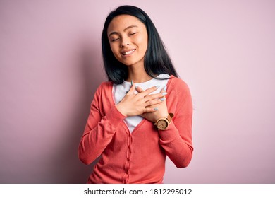 Young beautiful chinese woman wearing casual sweater over isolated pink background smiling with hands on chest with closed eyes and grateful gesture on face. Health concept.
