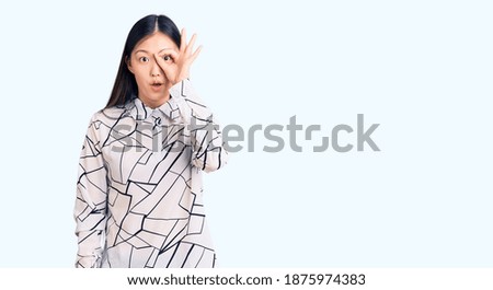 Young beautiful chinese woman wearing casual shirt doing ok gesture shocked with surprised face, eye looking through fingers. unbelieving expression. 