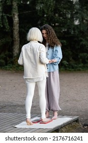 Young Beautiful Coach Helps Middle Aged Woman To Stand Barefoot On A Board With Nails. It Is Better If Someone Helps You Stand Up, Holding Hands. Board With Nails.