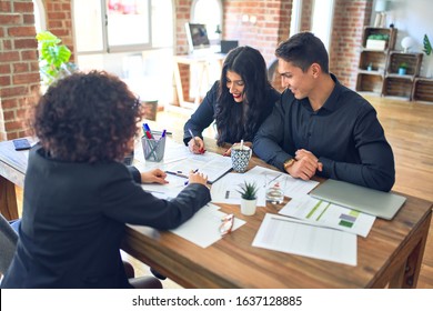 Young Beautiful Couple Applying For Mortgage. Sitting Smiling Happy Meeting With Real State Agent Signing Mortgage Loan At Bank