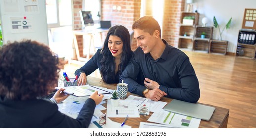 Young Beautiful Couple Applying For Mortgage. Sitting Smiling Happy Meeting With Real State Agent Considering Mortgage Loan At Bank