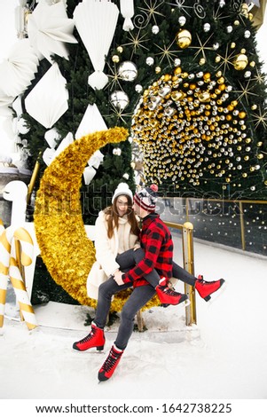 young beautiful couple boy in a red shirt and red hat girl in a white fur coat and white hat ice skating on an ice rink