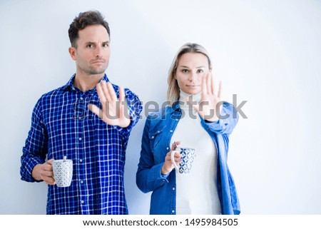 Young beautiful couple drinking cup of coffee standing over isolated white background with open hand doing stop sign with serious and confident expression, defense gesture