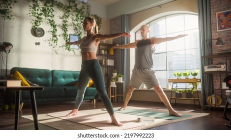 Young Beautiful Couple Exercising Together, Stretching And Practising Yoga In The Morning In Bright Sunny Loft Apartment. Healthy Lifestyle, Fitness, Wellbeing And Mindfulness Concept.