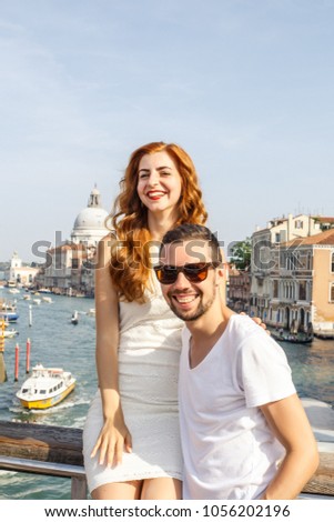 young beautiful couple, girl in white dress and man in white t-shirt stand against the background of the church of Santa Maria Della Salute city of Venice in Italy