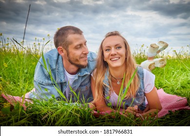 Young beautiful couple having fun on natural background. Date of guy and girl on a green field with glass in cloudy summer day. Yound family having rest together