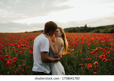 Young Beautiful Couple In Love Kissing On A Green Meadow Full Of Poppy Flowers. Loving Couple Hug One Another During Romantic Date In Poppy Field. Enjoying Time Together. Copy Space.