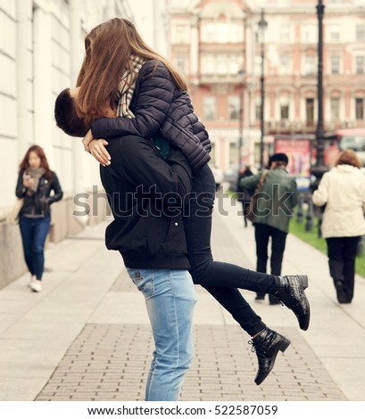 Young beautiful couple in love kissing and hugging at city street on autumn, fall, or spring day. Full length outdoors portrait. Lifestyle.